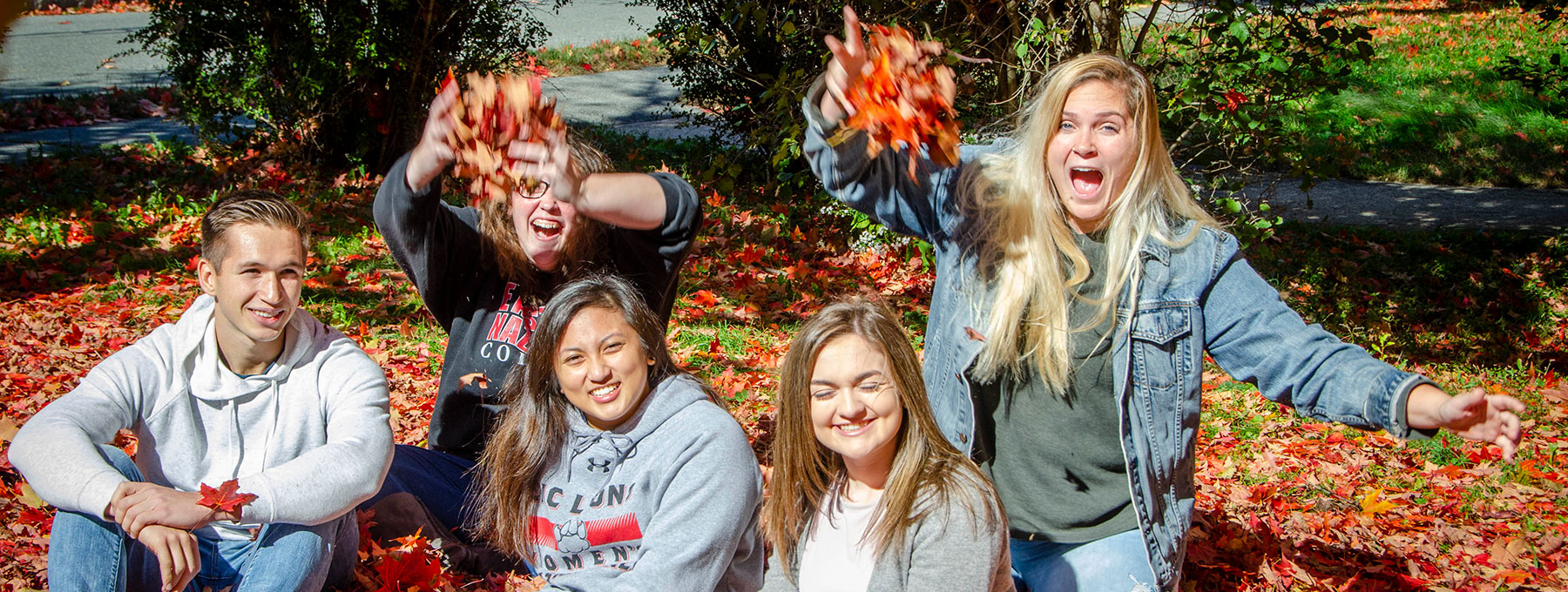 Admissions- students throwing leaves smiling