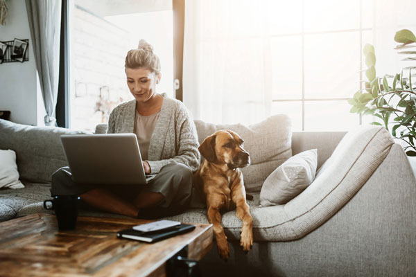 Woman working on laptop with her dog next to her