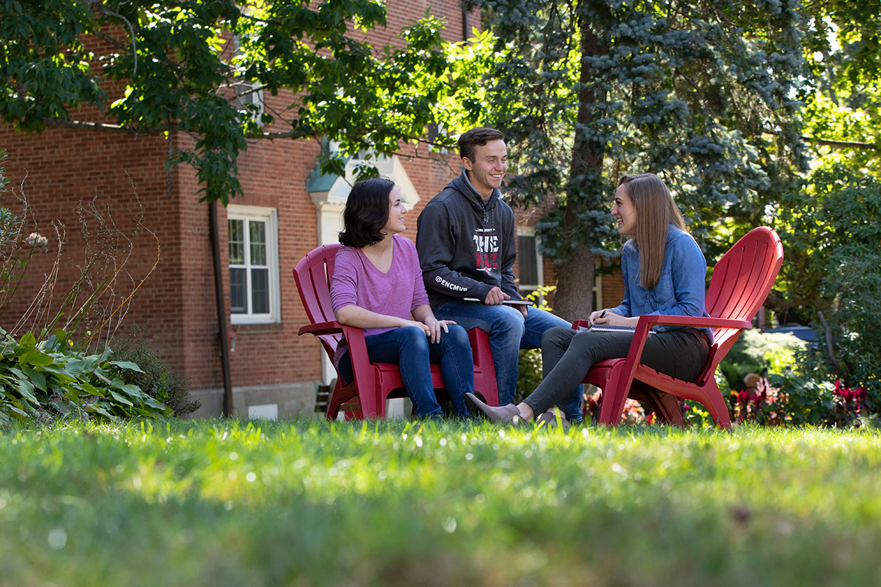 Three students gatherers on lawn chairs on the front lawn 