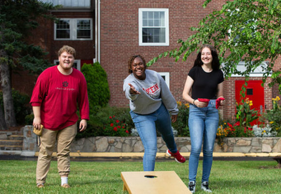 Three students laughing and playing Cornhole together 
