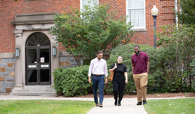 Three students walking down the sidewalk conversing with one another 